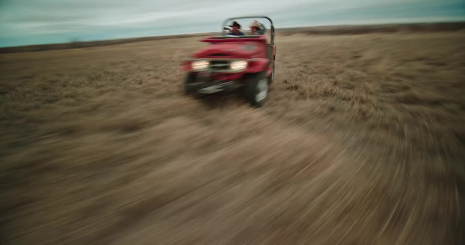 An aerial of a man and woman driving a jeep around a dry grassland in an open field
