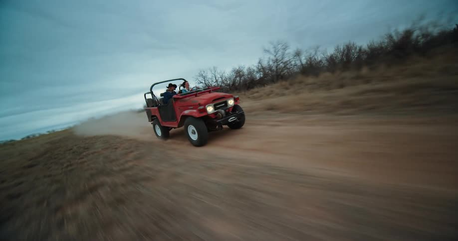 A pair of people ride in a jeep at a high rate of speed on a dirt road