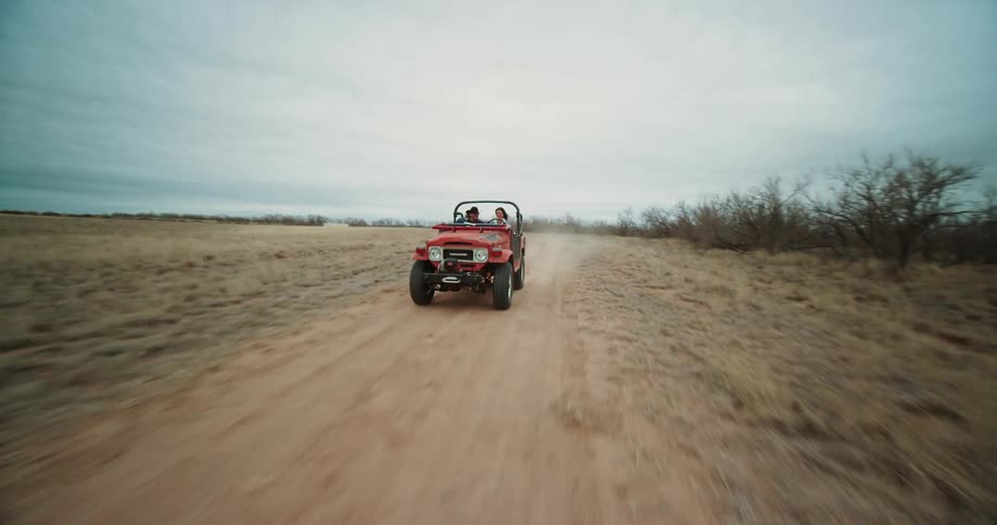 Intense twisting aerial view of a red jeep driving on a road in the desert at daytime