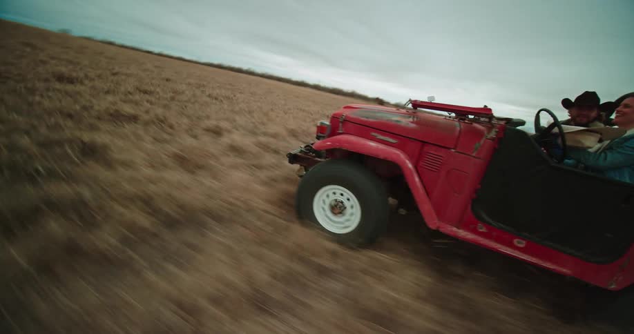 A man and woman have fun as they drive a jeep across a large field
