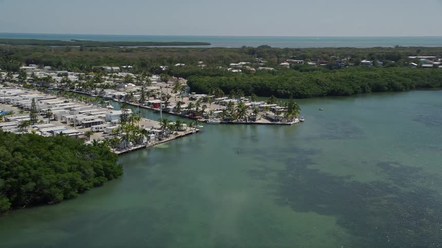 Aerial footage of Calusa Camp Resort in Key Largo Florida featuring boats sailing in the water near the resort with sparkling sunlight on the ripples and waves