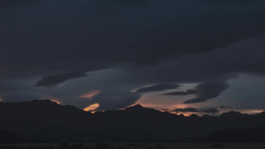 Sun casts reddish light across clouds as it sinks behind mountains