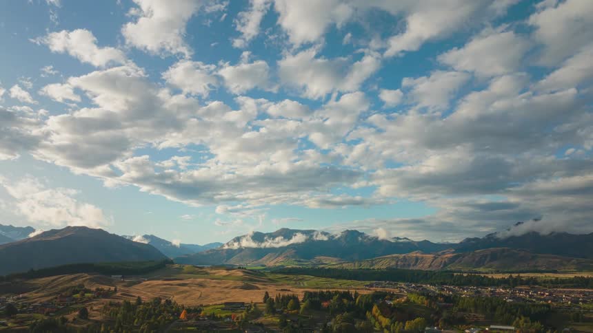 Cumulus clouds float across a blue sky over mountains and a rural community