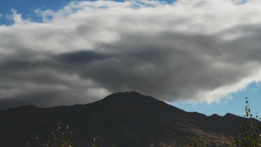 A time lapse of a large cloud over a mountain peak as it casts shadows over it