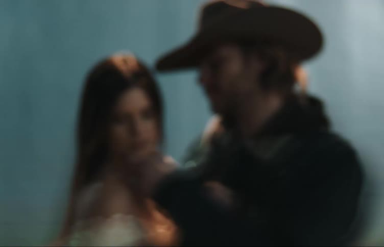Man with beard and brown hat looks at womans eyes lovingly and touches her chin