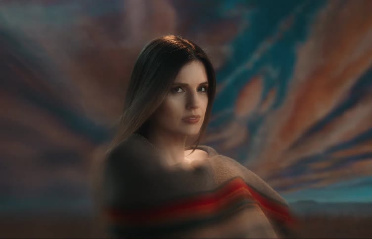 Woman wraps blanket around herself and poses against dramatic and scenic background