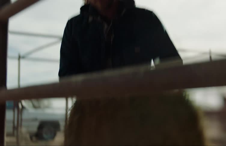 A man wearing a cowboy hat carries a bale of hay and sets it down near a fence and walks away