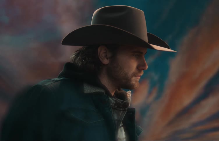 A man posing for a photo wearing a cowboy hat and looking straight forward before looking over at the camera