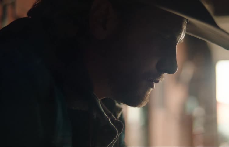 Cowboy sitting on a room muttering to himself stands up and walks away