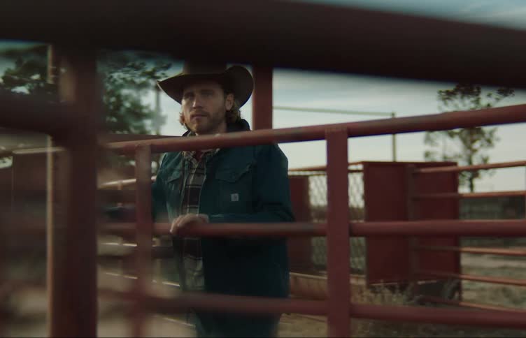 Man wearing cowboy hat opens gate on corral