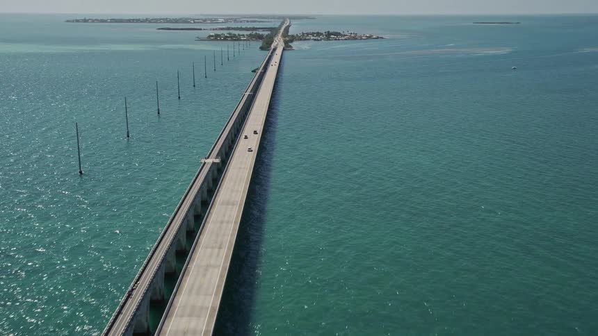 Aerial footage of driving along Overseas Highway towards Conch Key in Marathon Florida with a side view of the highway bridge and the Atlantic Ocean in the background
