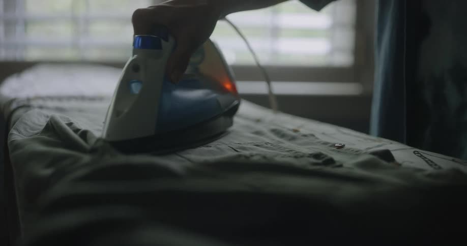 A person using a hot iron on a shirt on the ironing board before stopping
