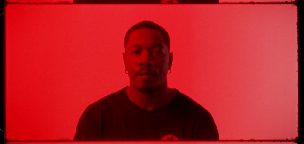 A black man staring projected onto a red painting working as a screen