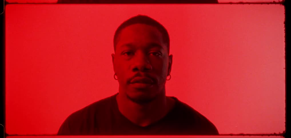 A man poses in a studio against a red background