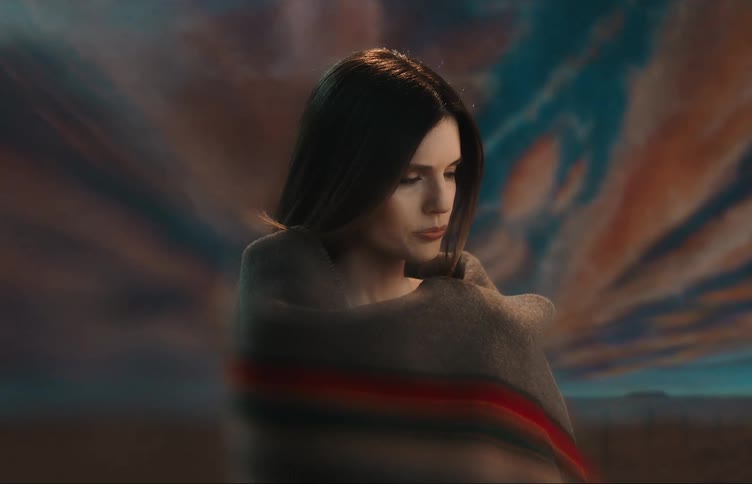 Woman warps herself in blanket while posing against vibrant and scenic background