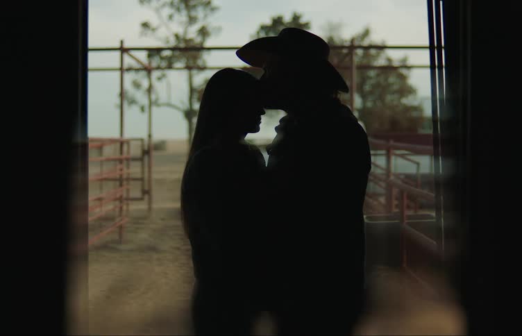 A couple embraces in silhouette in a doorway as he kisses her forehead tenderly
