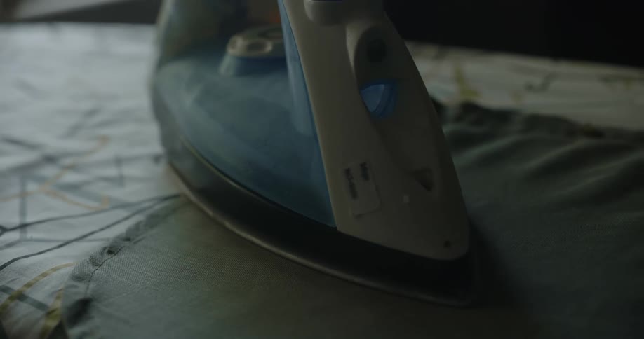Steam rises from an iron placed on denim on an ironing board