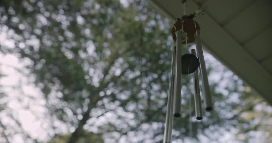 A wind chime gently sways in the breeze as it hangs from a building