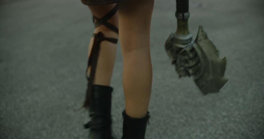 A person walking down a road carrying a medieval weapon while wearing a strap around their leg