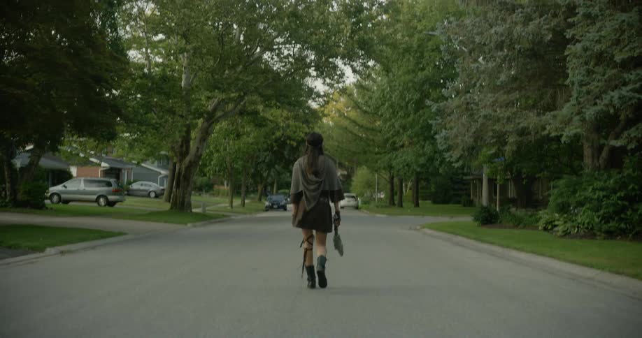 A young woman is slowly walking down the middle of a neighborhood street in the summertime