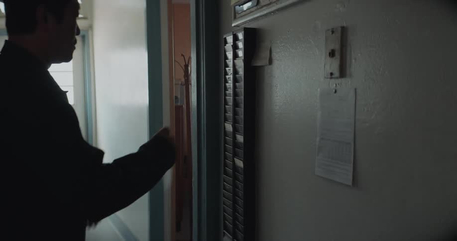 A man takes a printed card out of a rack on the wall and walks into a room after looking it over