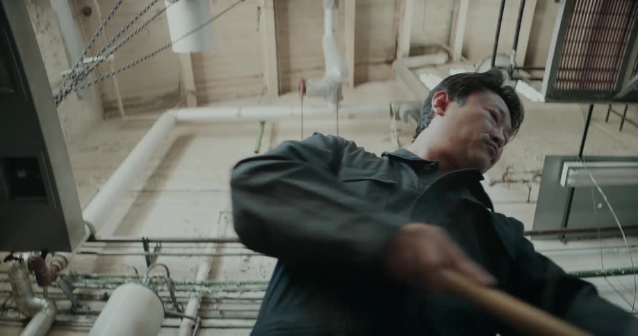 A man is mopping the floor inside a facility with pipes behind him