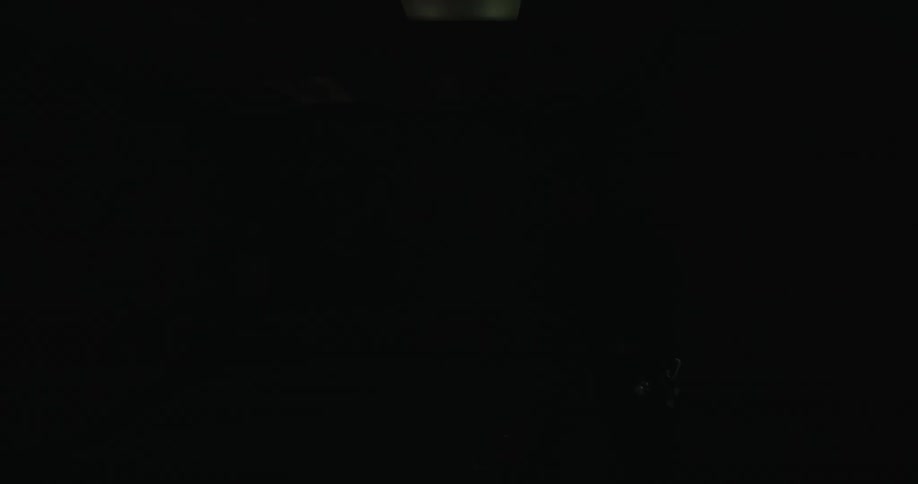 A man is wearing headphones as he vacuums a room with wood paneling and a forest picture on the wall and the ceiling lights are flashing off and on