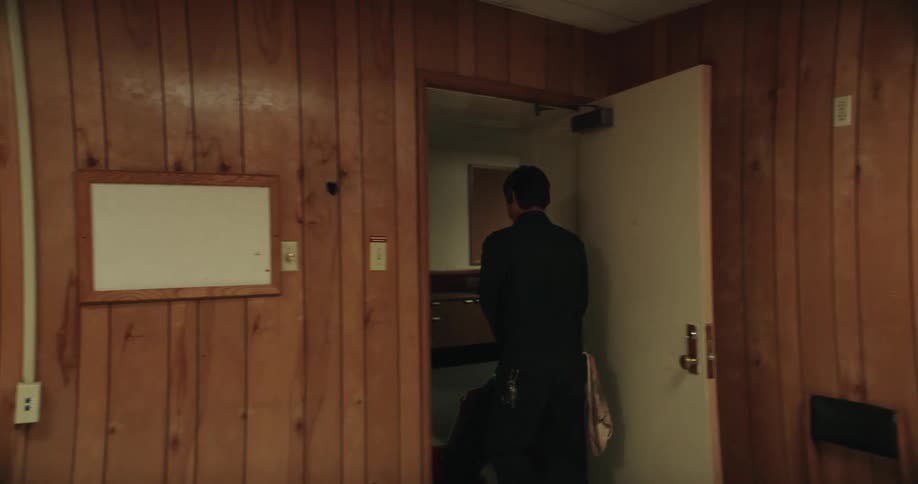 Man wearing headphones walks out of a dark doorway into another room