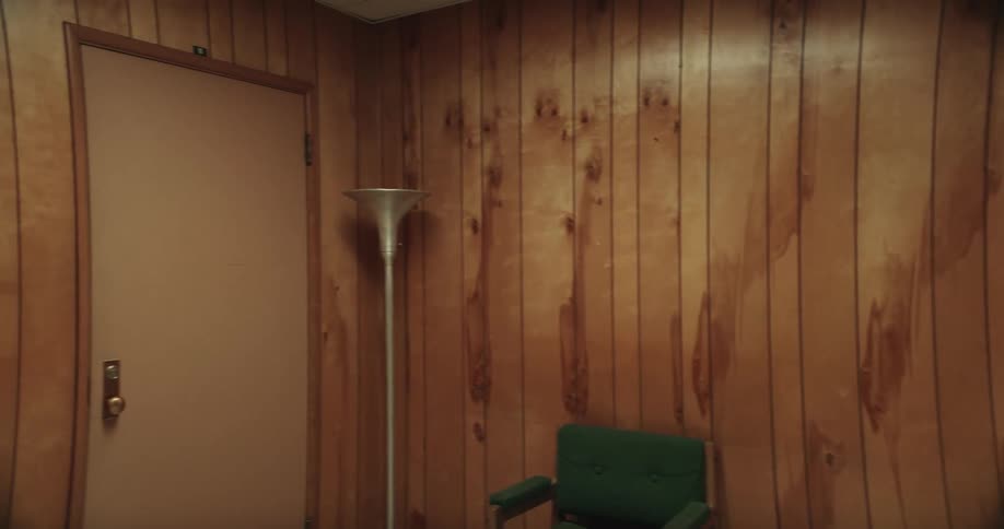 Camera pans left revealing empty office space with wood paneling and a janitor mopping one of the rooms