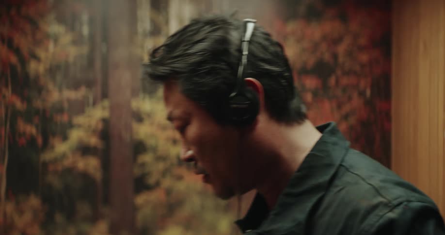 Man wearing headphones vacuums a room in front of a mural of trees