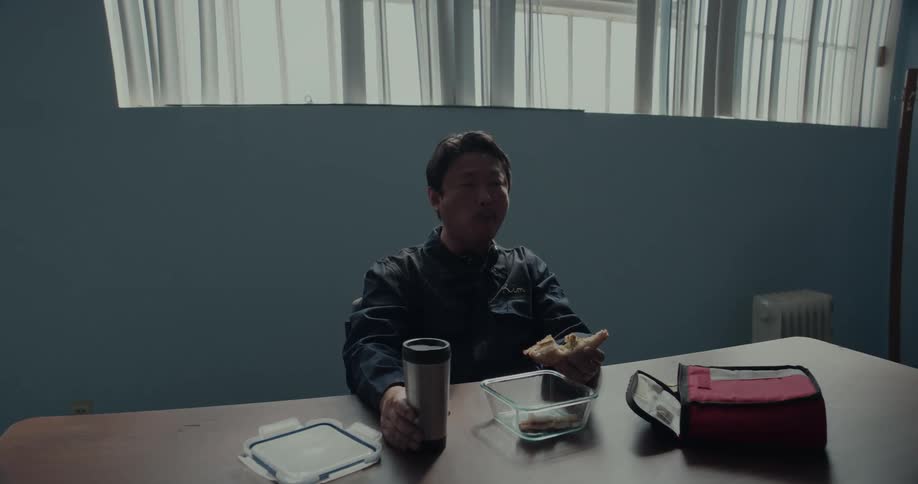 Man sits alone in room eating a sandwich from a packed lunch