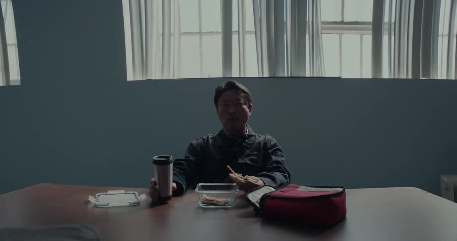 Man sits at table under a row of windows and drinks from a cup