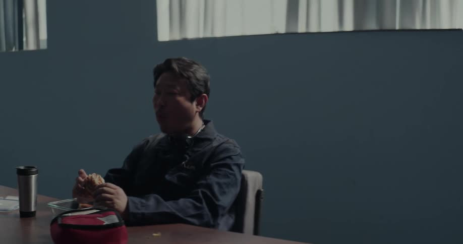 Male cleaner sits at table eats a sandwich in the building
