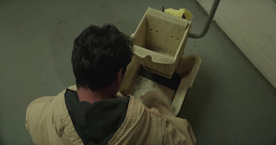 A man is standing over a mop bucket as he bends down and reaches inside it