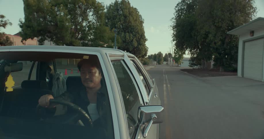 Man drives a car down a rural street passing trees midday