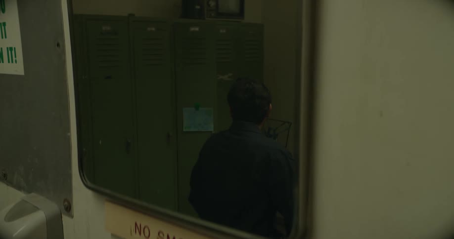 The reflection of a man sitting down putting on his coat and walking away is seen in a mirror