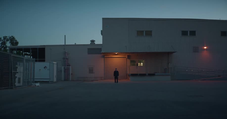 Person stands outside of a building near an empty lot at dusk