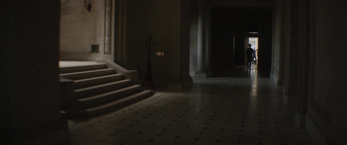 People walk outside down the dark hall
