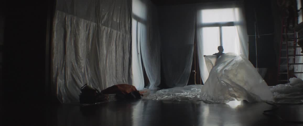 A man unfolds a plastic sheet and drags it across the room
