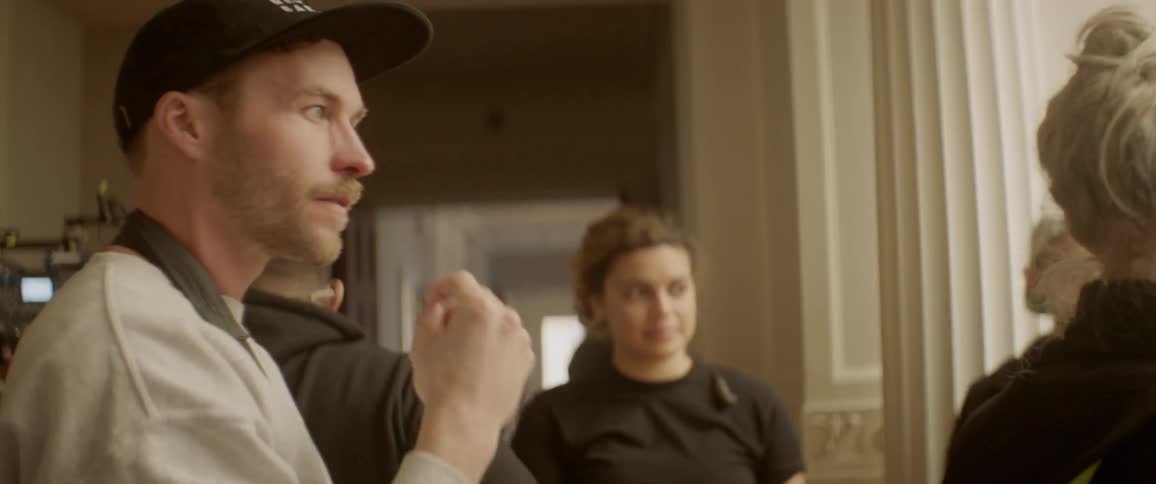 Man talks to people and waves his hand in front of his face