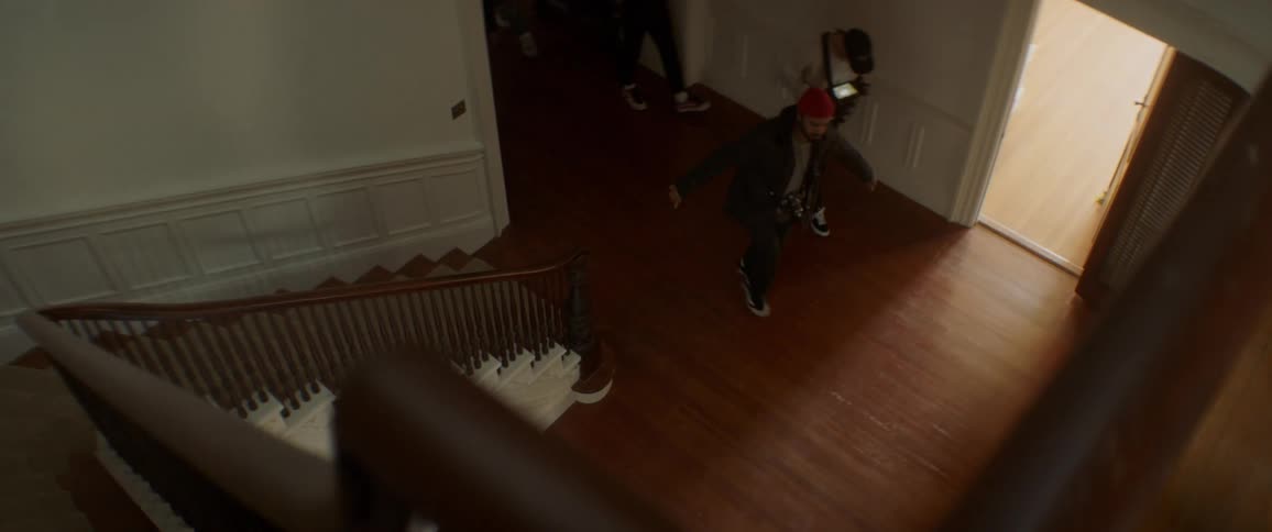 A man stumbles across a foyer followed by a film crew and camera