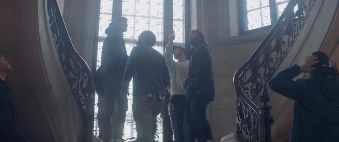 Men walk up steps and stop on the landing as a person talks and points