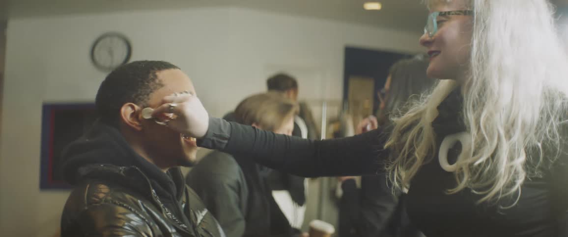 A man smiles as a makeup artist applies make up