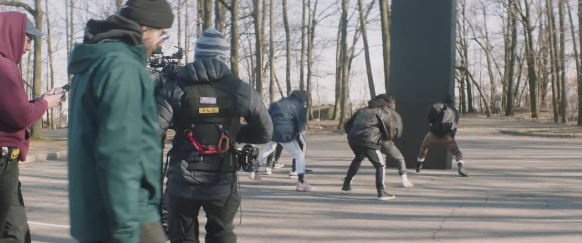 A cameraman and crew film people dancing on an outdoor set