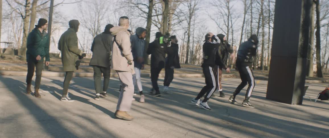 Men dance in a parking lot as others walk through and film them