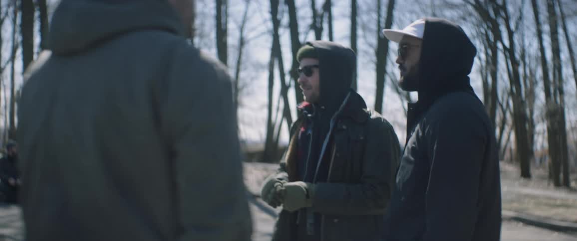 Several people stand outside in the woods talking on a cold day