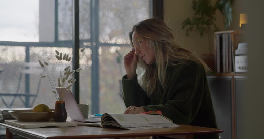 Blonde woman sitting at the table takes a break and looks out the window
