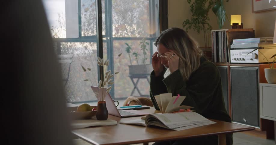 Blonde woman sitting at the table wears her glasses and uses the laptop