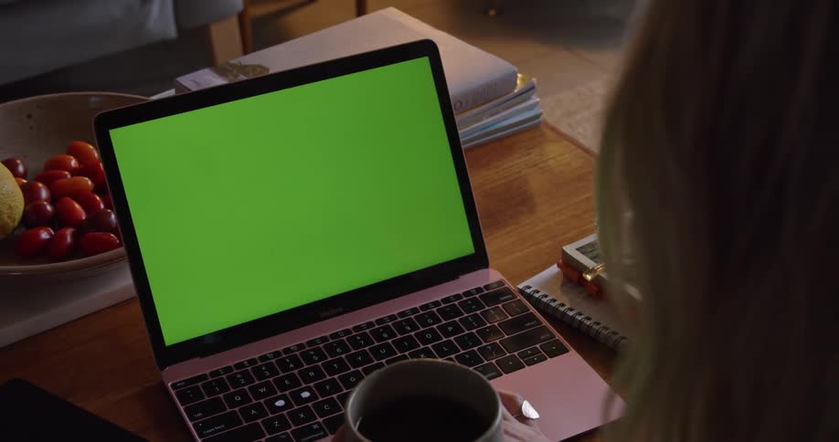 Woman sitting at table uses laptop while drinking a cup of coffee