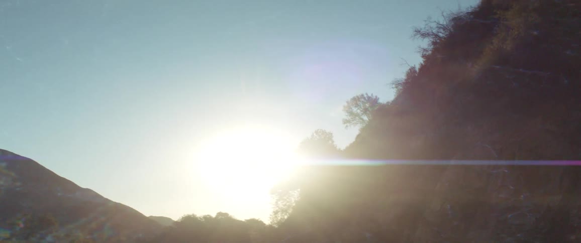 The sun shines high in the distance amongst some shadowy mountains